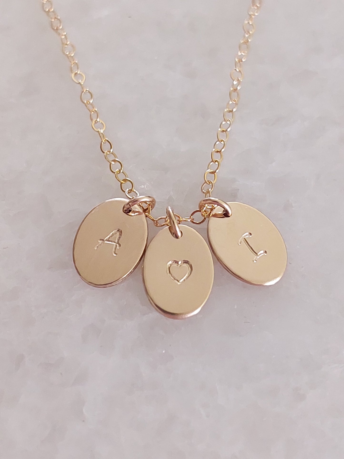 Gold necklace with three personalised small oval pendants on a light gray background
