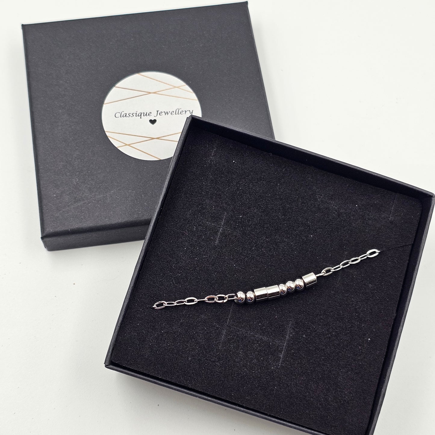 A personalised sterling silver beaded chain Morse Code bracelet displayed inside an open black presentation box, with the matching closed box and circular Classique Jewellery label visible behind it on a light background.